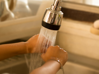 Photo of a child washing a dish as water sprays from the tap at the sink.