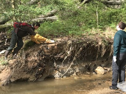 Two people pick up garbage from a stream