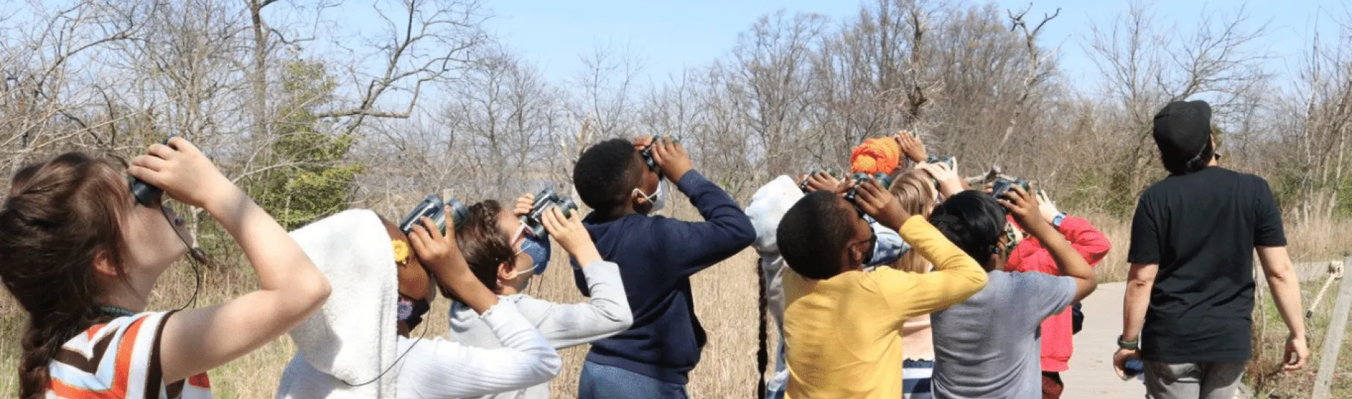 Photo of students looks up at the sky with binoculars