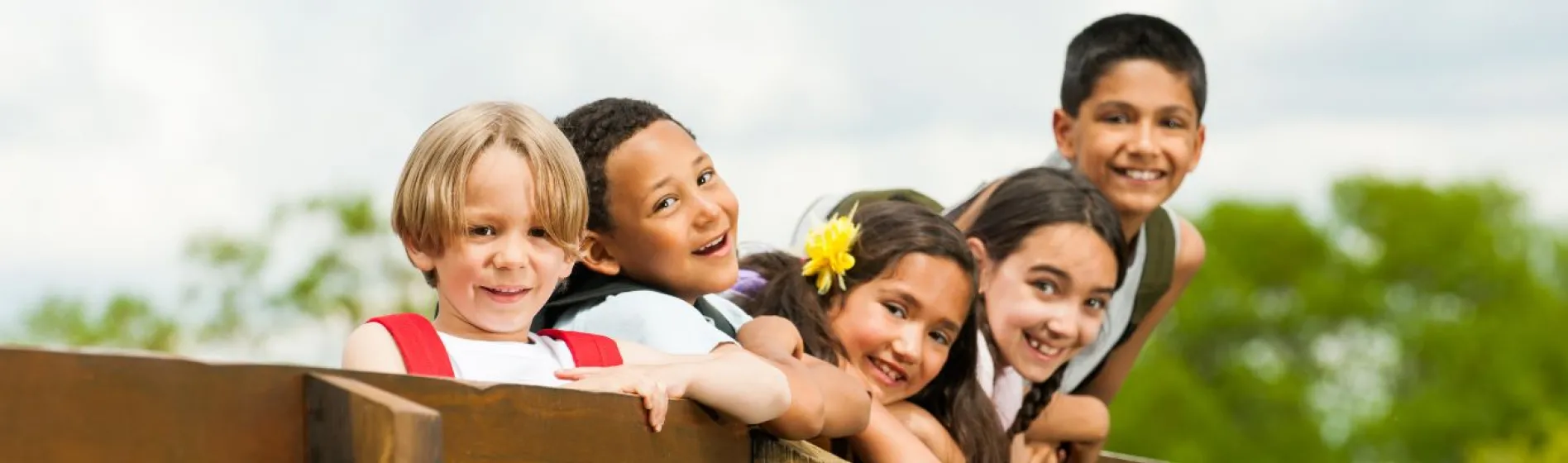 a group of middle school kids leaning over a railing and smiling outside in the sun