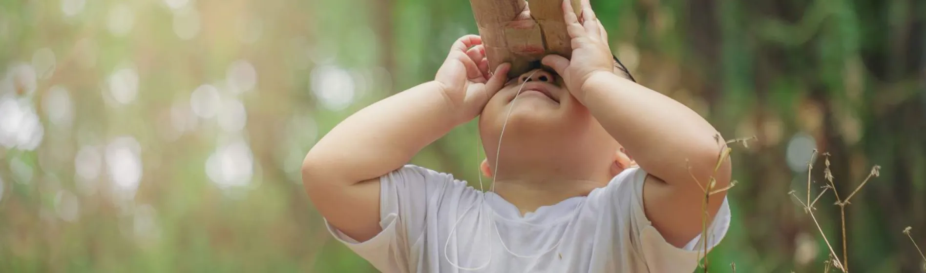 Young child outdoors with paper bionoculars looking up 