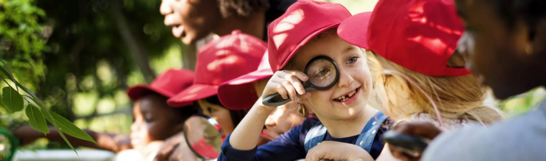 Child looking through a magnifying glass at others.