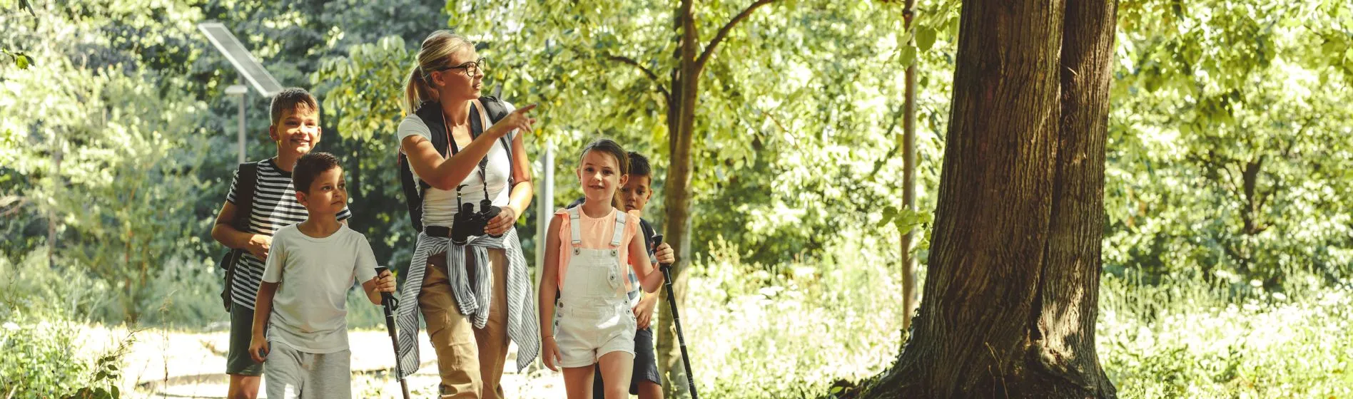 An outdoor educator walks on a trail with a group of students while pointing out something in nature