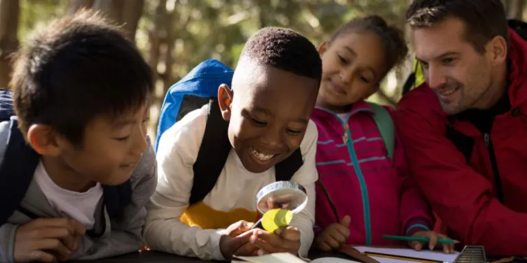 Group of students looking at plants through a magnifying glass during an outdoor environmental education activity