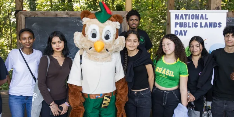 a diverse group of youth stand with Forest Service mascot Woodsy the Owl on National Public Lands Day