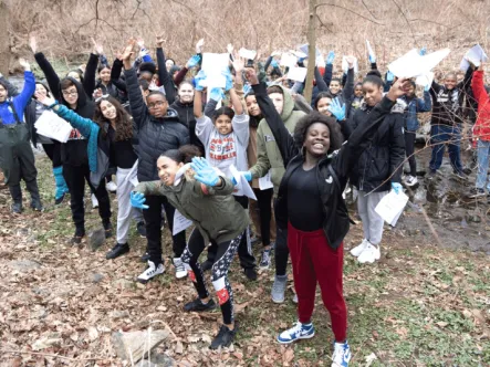 Students standing outside near stream with hands up celebrating the completion of Greening STEM program