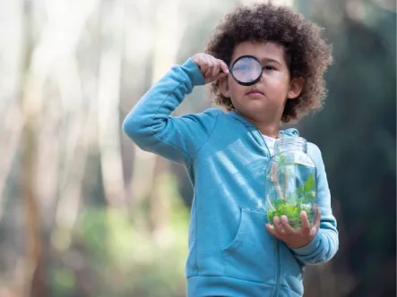 a child holds a jar of water looking through a magnifying glass