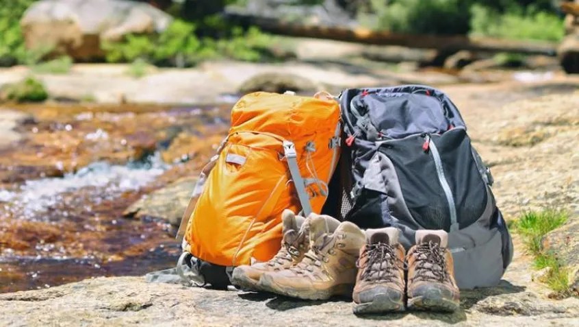 backpacks and hiking boots on a rock near water