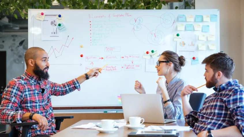 Photo of diverse group of professionals talking around a whiteboard.