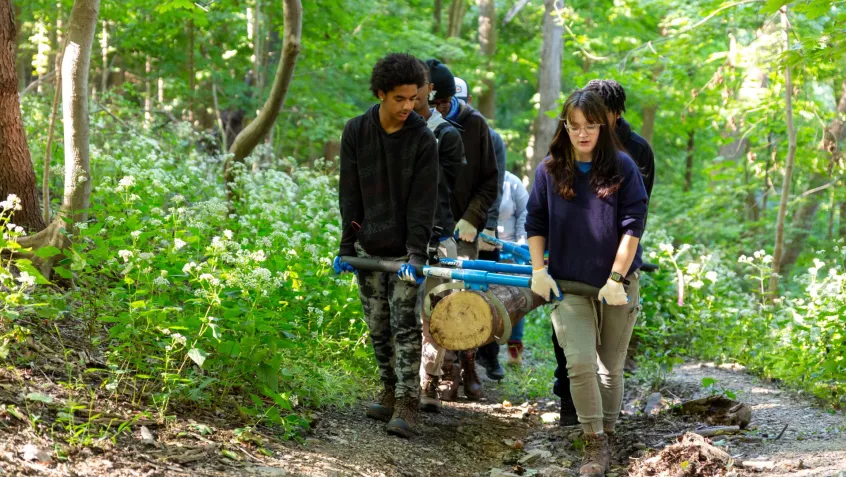 A diverse group of young people carry a large log to place on trail during National Public Lands Day event.