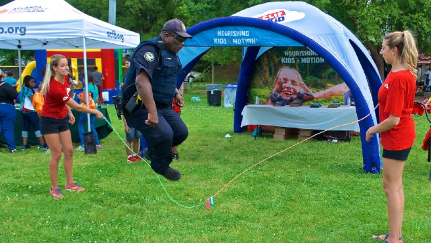 Police officer jumping rope being held by two volunteers