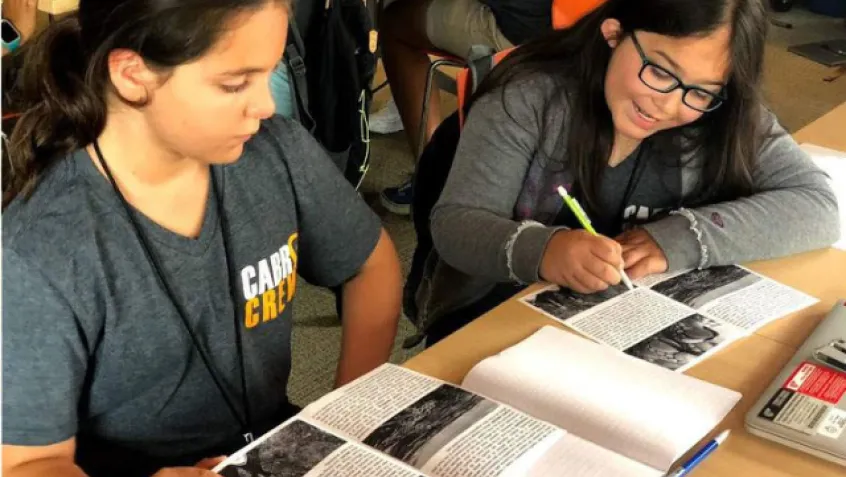 Two girls sitting at a desk looking at books together