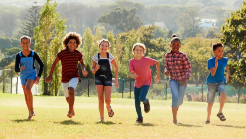 Kids running outdoors in a line towards the camera smiling