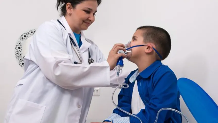 A female doctor holds an oxygen mask up to the face of a little boy