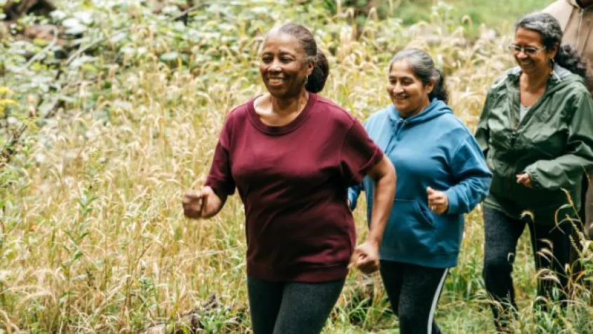 A group of older people walk on a path through a forest