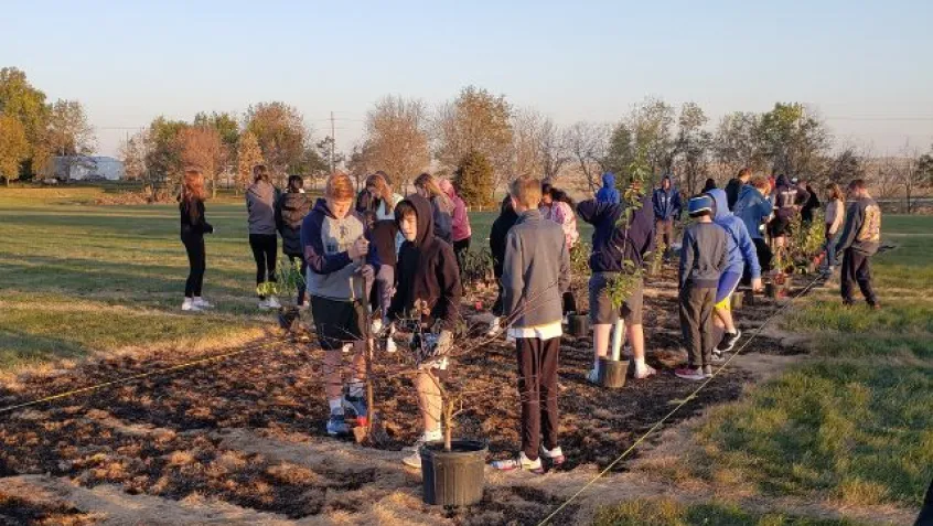 Students from Quad Cities Iowa plant native trees during a Greening STEM project in prairie 