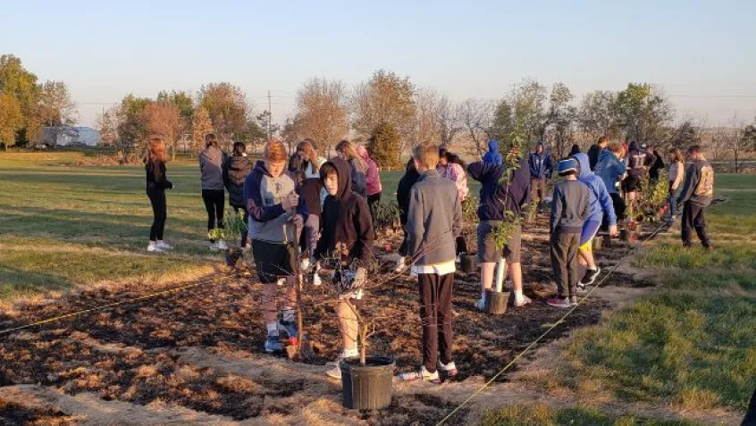 Students from Quad Cities Iowa plant native trees during a Greening STEM project in prairie