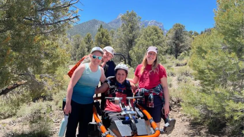 a woman site in an all terrain wheelchair surrounded by a group of people on the trail
