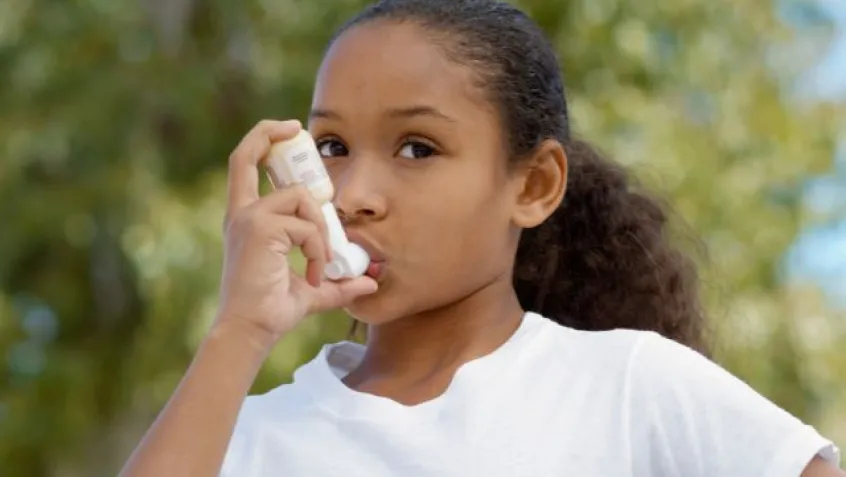 young girl using asthma inhaler outside