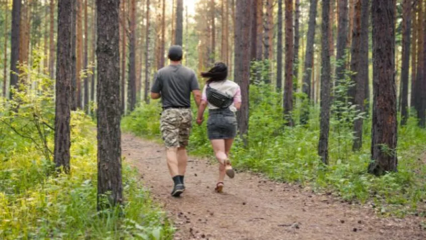 a man in camo shorts holds hands with a woman as they walk through the forest