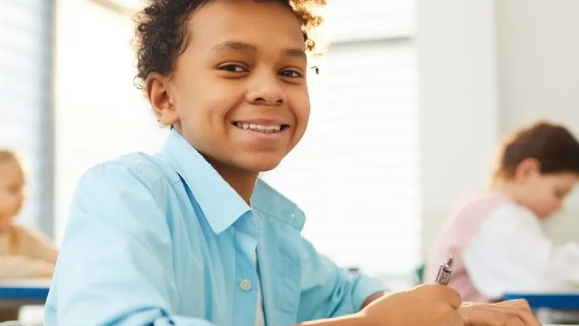 a middle school student smiles while sitting at a desk