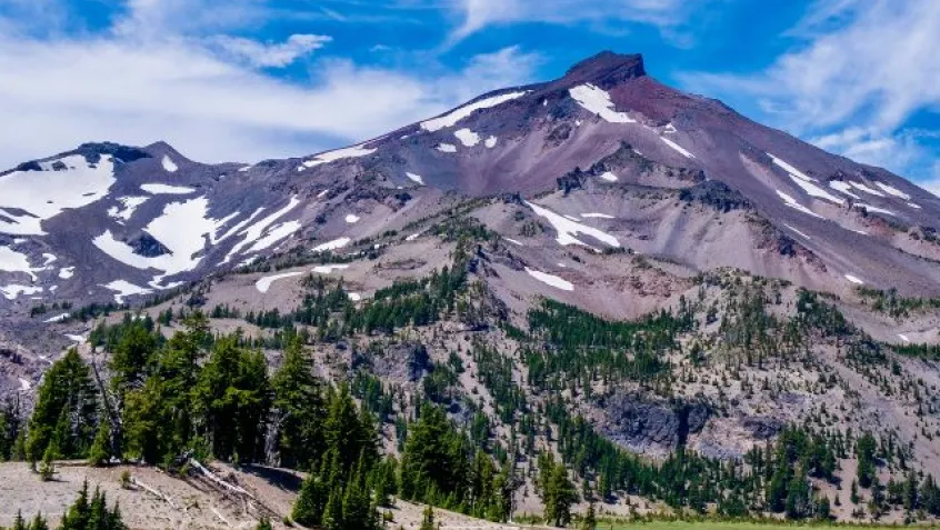 small patches of snow sit on the side of a mountain top with exposed dirt