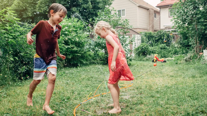 Two children playing with a sprinkler in their backyard.
