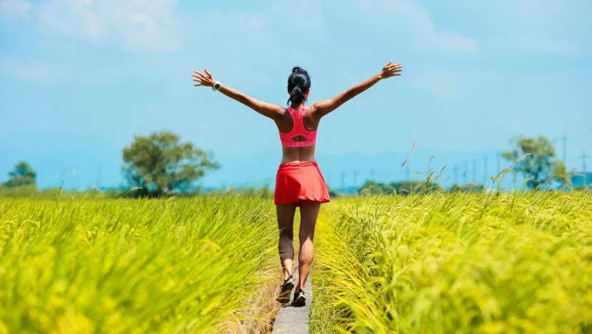 A woman walking in a green field with her arms open wide.