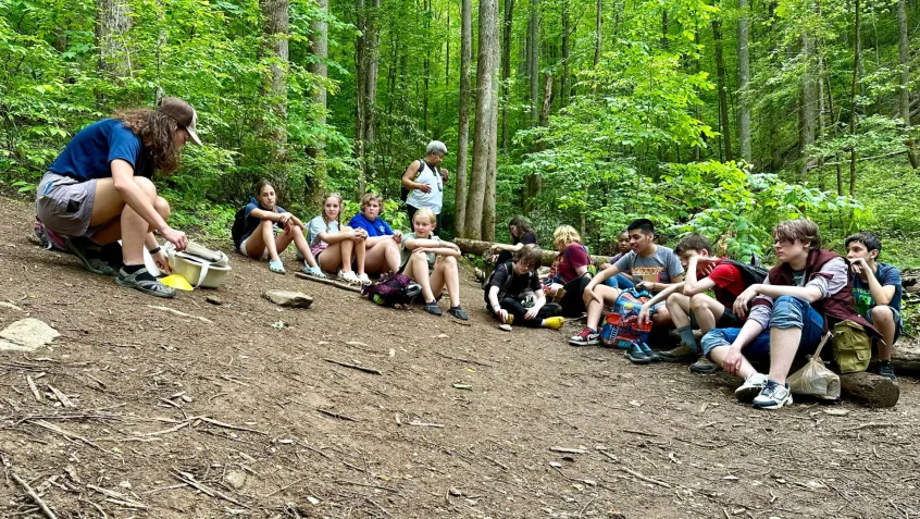 a group of students sits on the forest floor for a Greening STEM outdoor education lesson