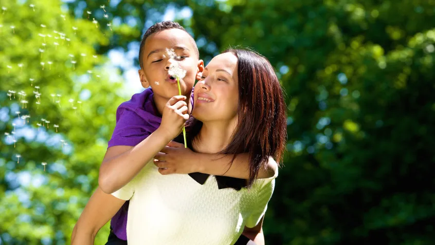 Boy blowing a dandelion with his mom