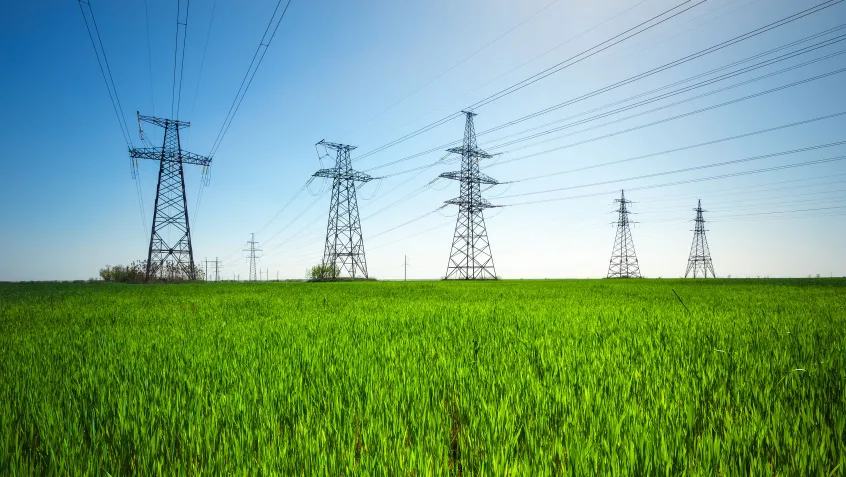 HIgh voltage lines and power pylons in a a green agricultural landscape with a blue sky on a sunny day