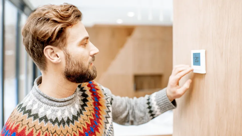 Man in sweater adjusting thermostat