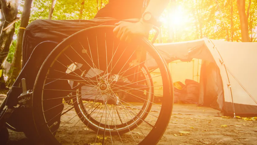 man in wheelchair next to a tent in the forest