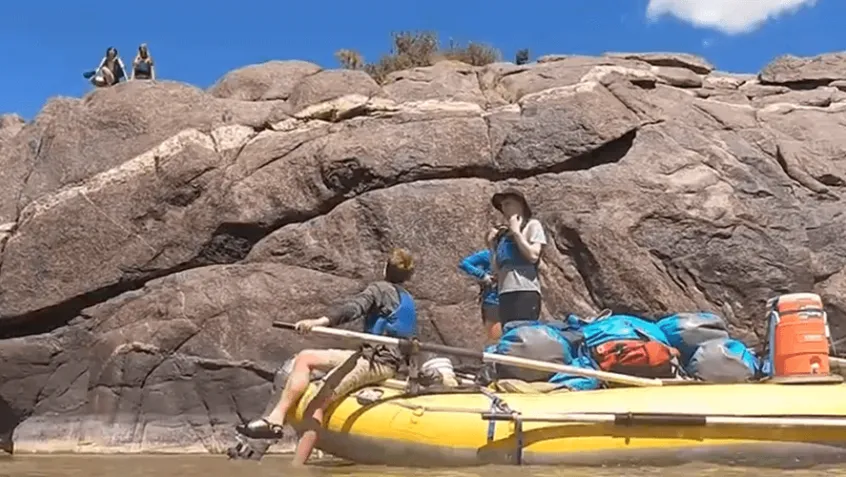 Student on raft next to big canyon rock during experiential education trip