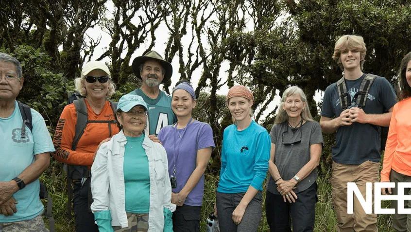 group of women and men part of the Army Natural Resource Program standing together smiling outside in front of trees and bushes.