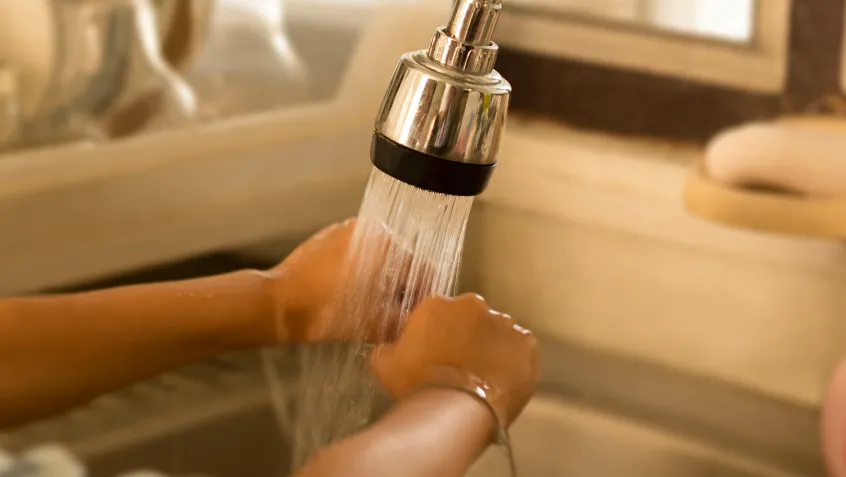 Photo of a child washing a dish as water sprays from the tap at the sink.