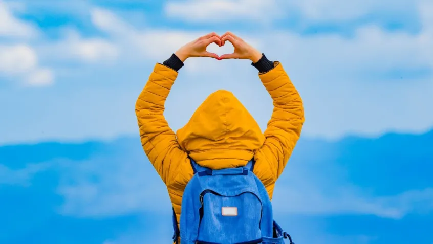 person standing in front of distant mountain range making heart shape with hands