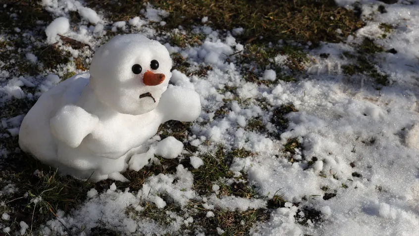 snow man melting in warm winter surrounded by patches of grass