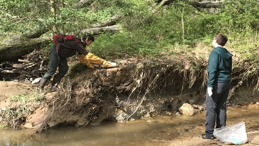 Two people pick up garbage from a stream