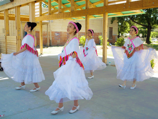 Women in traditional Mexican dress dancing inside an outdoor pavillion