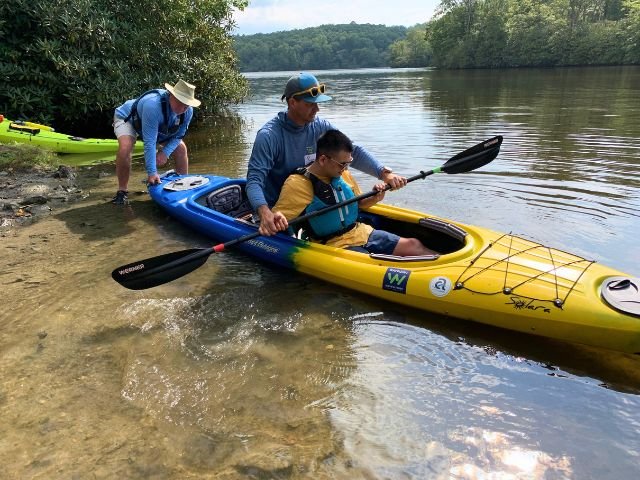a man helps young man use a kayak paddle
