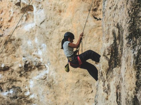 a young woman climbs a mountain with climbing equipment