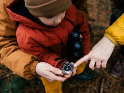 a young boy uses a compass with the help of adults