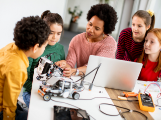 Teacher surrounded by 4 children and computer and electronic car on the table