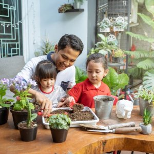 a father works with his daughter to pot a plant in the living room