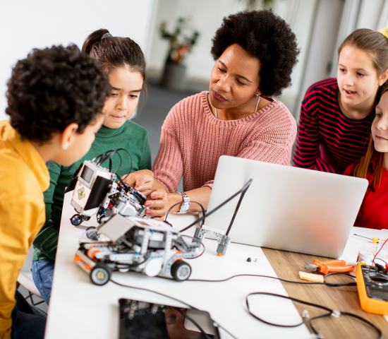 Teacher surrounded by 4 children and computer and electronic car on the table