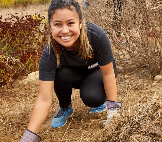 Young woman with gloves smiling and removing weeds