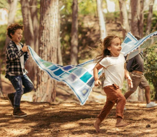 Two children holding a blanket up and running through the forest