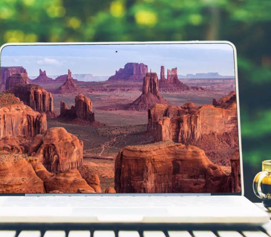 Laptop with canyonlands on screen sitting outdoors on table with coffee cup next to it