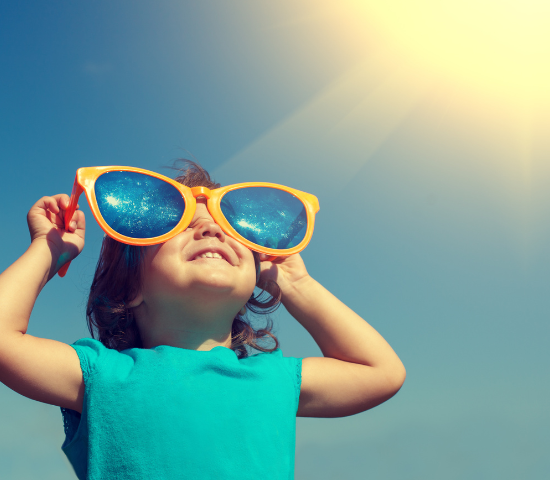 Young child holding large sunglasses over their eyes and looking towards the sun